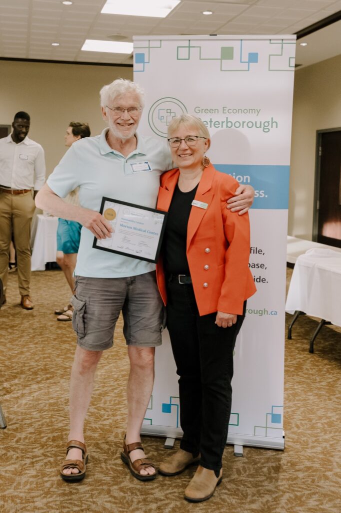 Guy Hanchet of Morton Medical Centre holding the 2026 Sustainability Catalyst Award certificate, standing with a Green Economy Peterborough representative in front of a Green Economy Peterborough banner